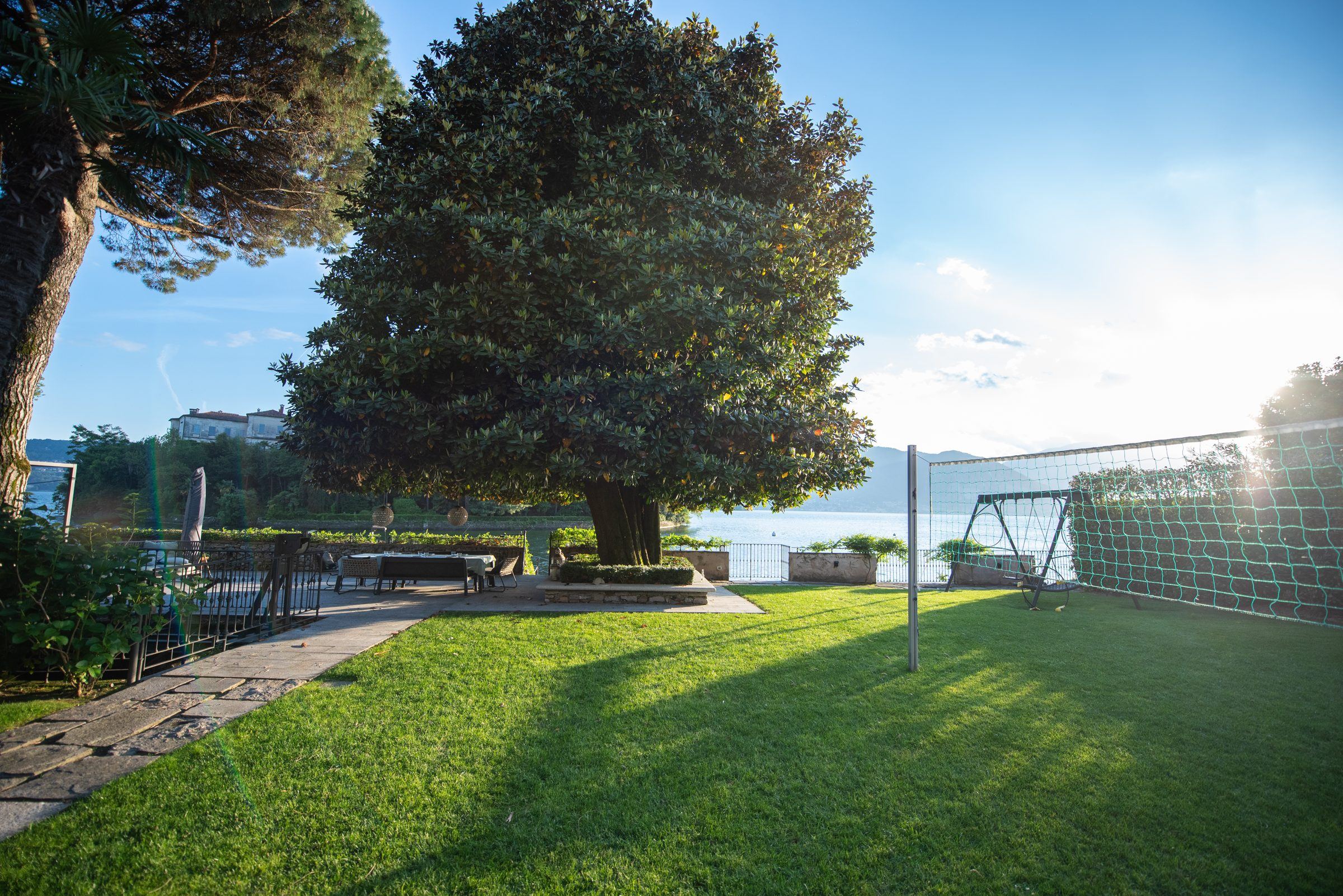 Sonniger Garten mit großer Magnolie, dahinter der Lago Maggiore und die Berge