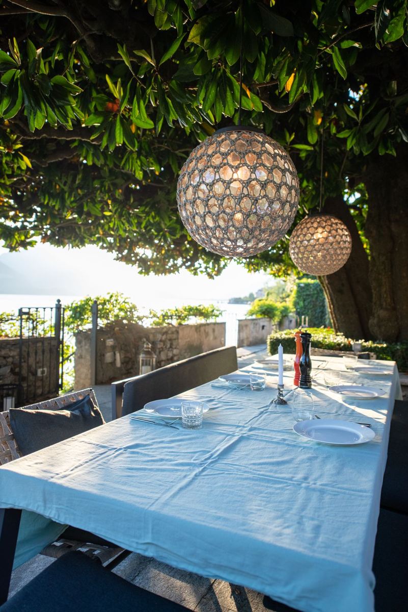 Gedeckter Tisch unter der Magnolie mit Laternen, dahinter der See
