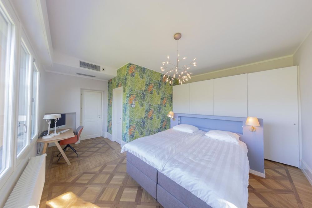 Schlafzimmer mit Dschungeltapete, Schreibtisch und Fensterfront
