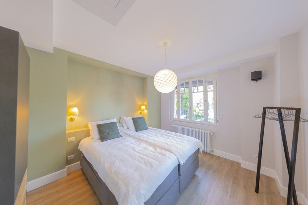 Schlafzimmer mit salbeigrüner Wand und Bogenfenster zum Garten